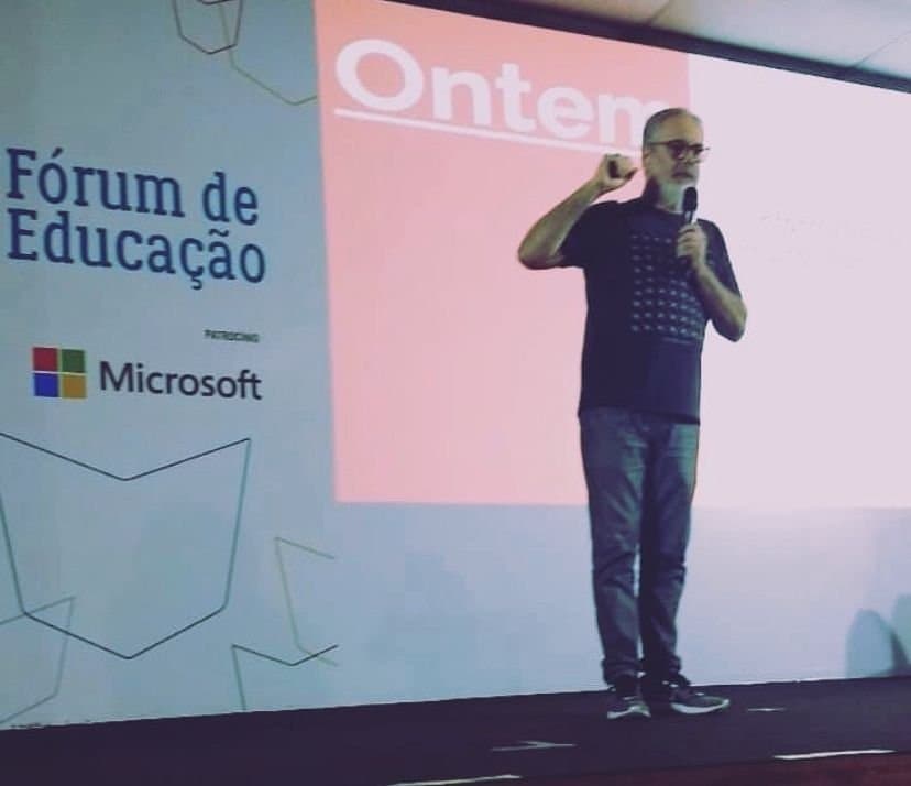 Ruy Jobim de microfone na mão, no palco do Fórum de Educação da Bienal do Livro, com o telão ao fundo
