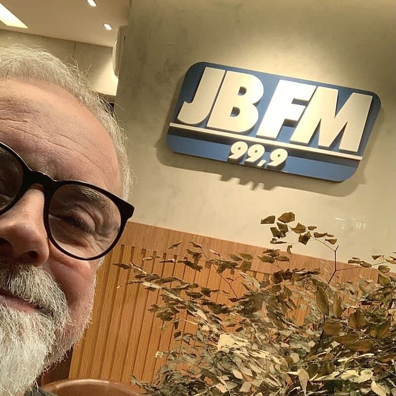 Selfie de Ruy Jobim na recepção da JB FM 99,9, com o logo da rádio ao fundo
